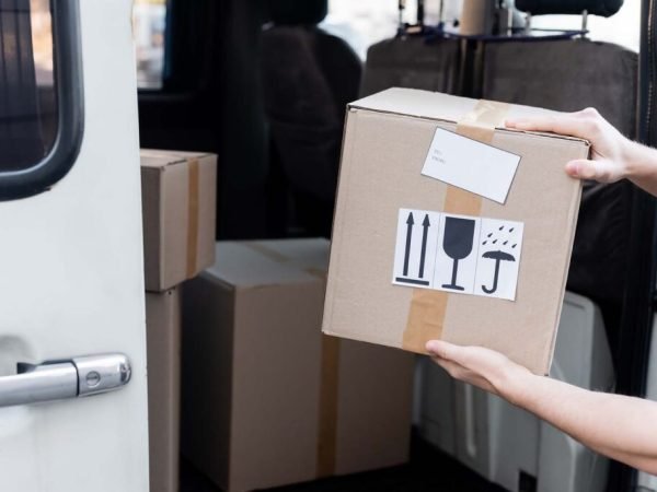 Cropped view of courier holding carton box with signs near car outdoors